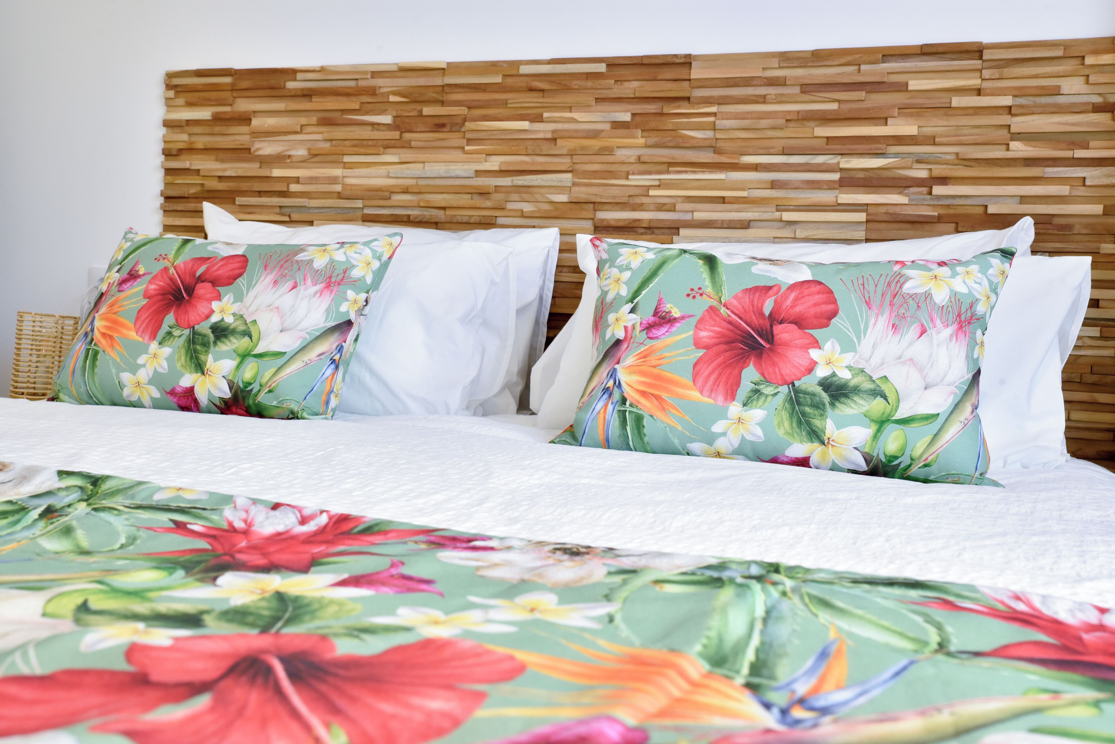 Un lit avec une couvre-lit à motifs floraux et deux oreillers à imprimé tropical.