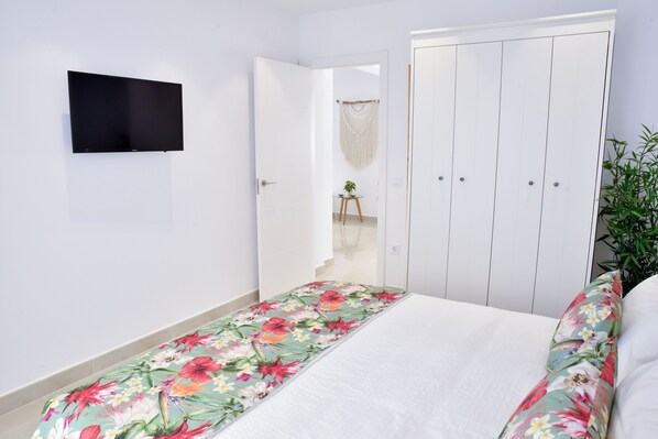 A bedroom with a bed, a TV mounted on the wall, a wardrobe, and a small table with a plant.