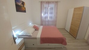 Un dormitorio con una cama, una mesita de noche, un armario de madera y una ventana con cortinas translúcidas.