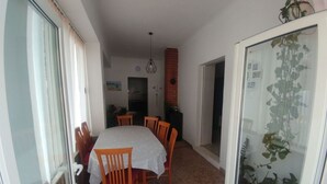 Un comedor con mesa y sillas, una cocina al fondo y una puerta de cristal con una planta.