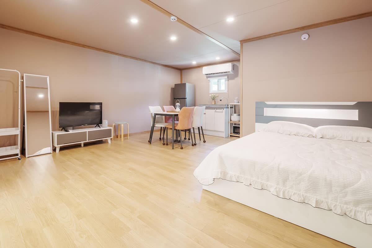 A modern hotel room with a large bed, a desk with a chair, a television, and a wardrobe.