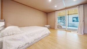 Ein Schlafzimmer mit Bett, Nachttisch, einem Fenster mit Vorhängen und Blick ins Freie.