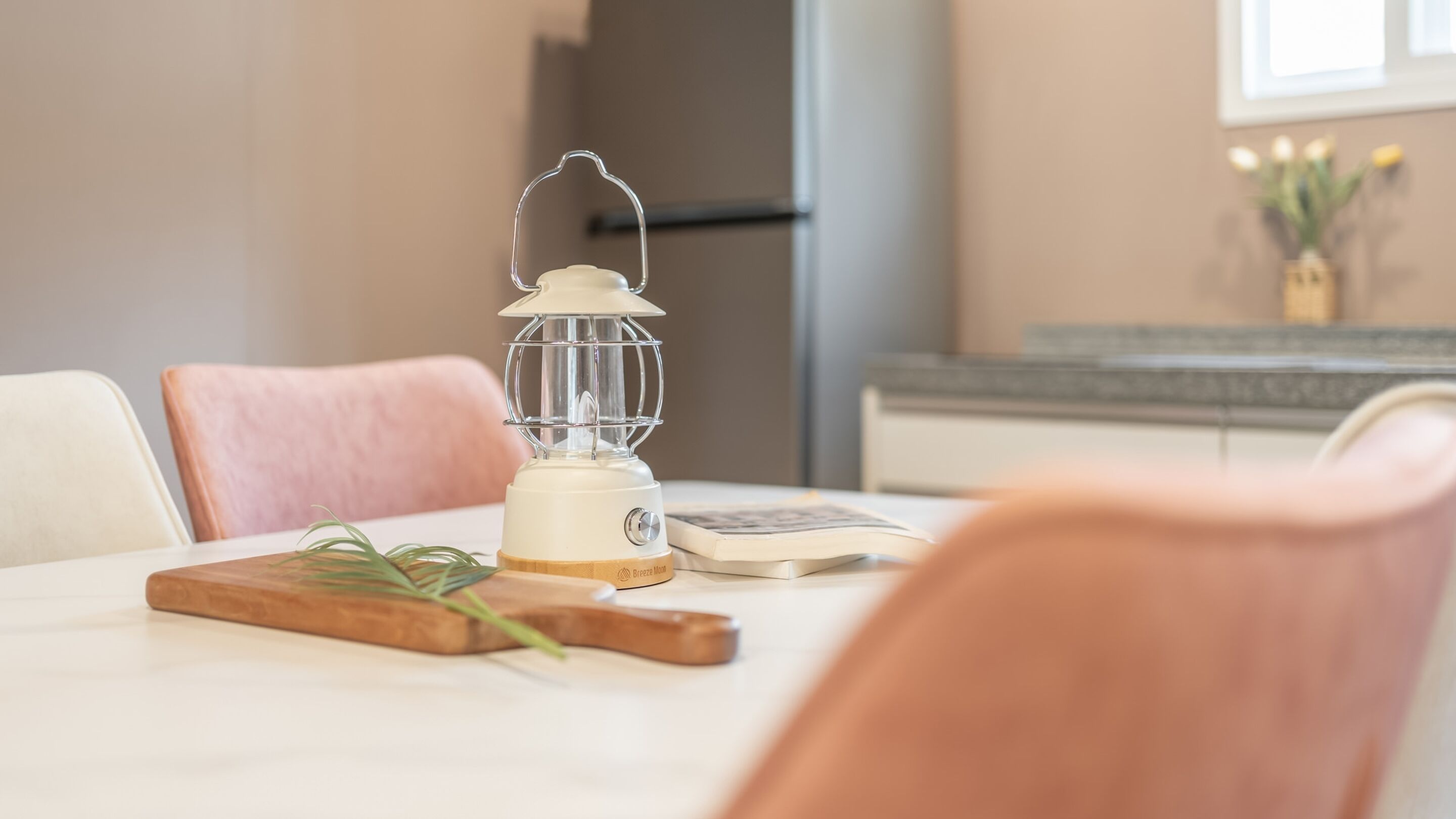 A table with a white table lamp, a book, and a wooden cutting board with a plant.