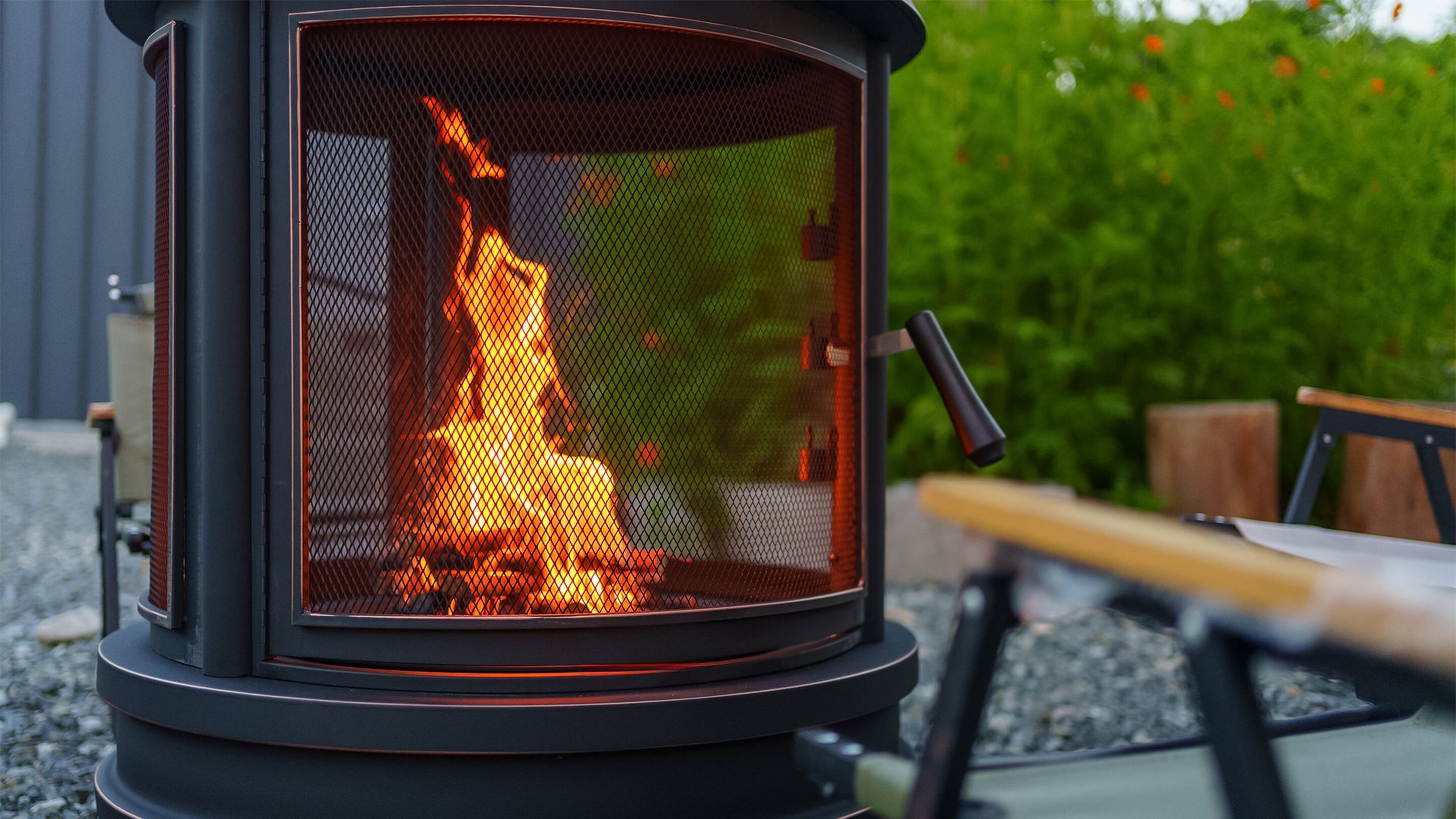 A wood-burning stove with a mesh front, set outdoors on a gravel surface.