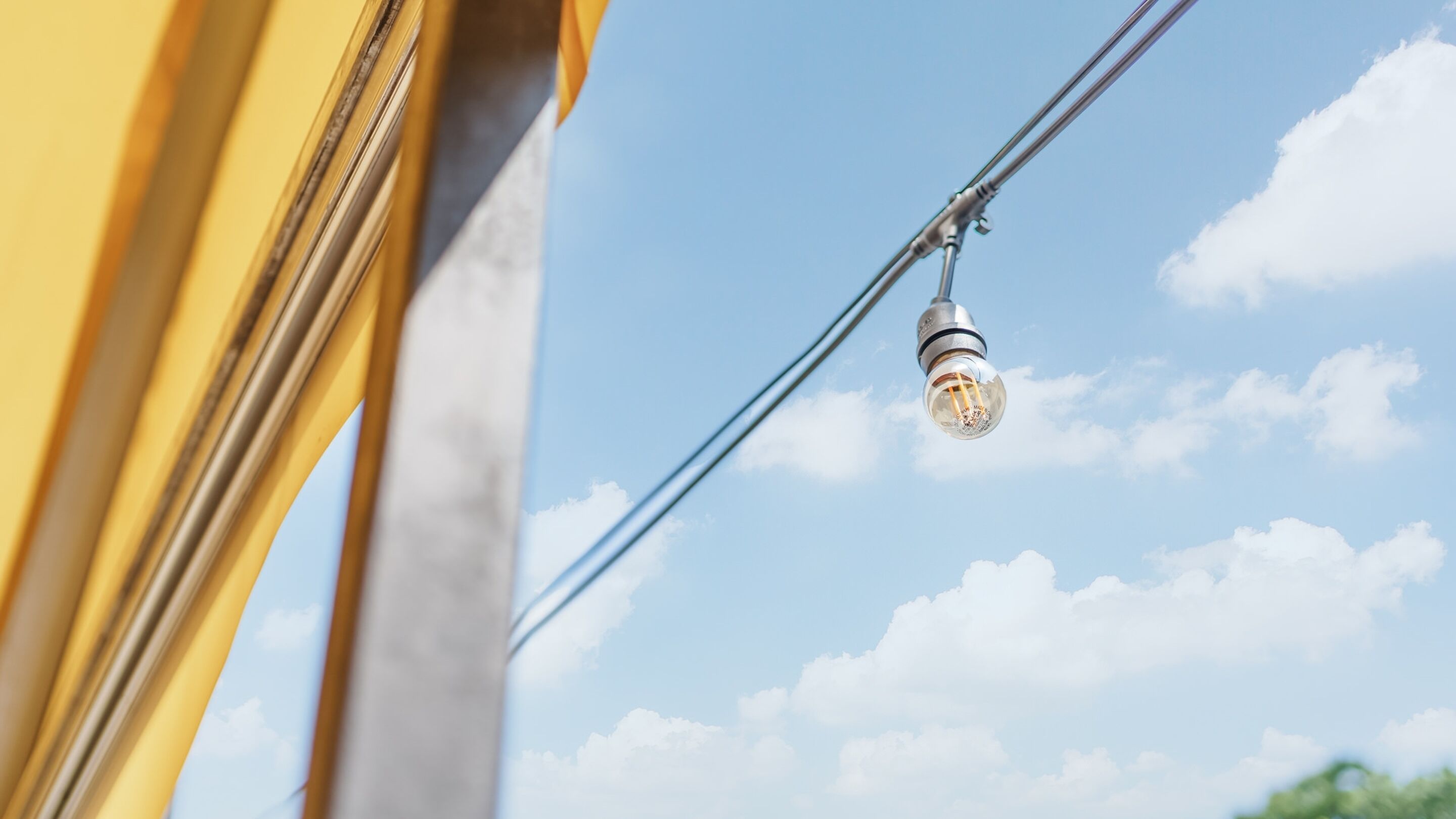 Un primo piano di una lampadina appesa a un filo su uno sfondo di cielo sereno.