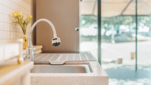 Eine moderne Küche mit Armatur aus Edelstahl, einer weißen Arbeitsplatte und Blick auf einen Pool durch große Fenster.