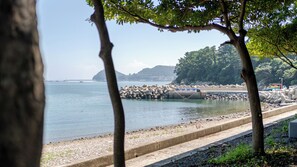 A coastal view with a clear sky, calm sea, and a rocky shoreline with a concrete barrier. - Namhae Chojun Bada Forest Glamping (Namhae)