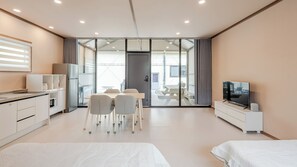A modern hotel room with a kitchenette, a dining area with chairs, a TV, and a large sliding glass door leading to an outdoor patio. - Namhae Chojun Bada Forest Glamping (Namhae)