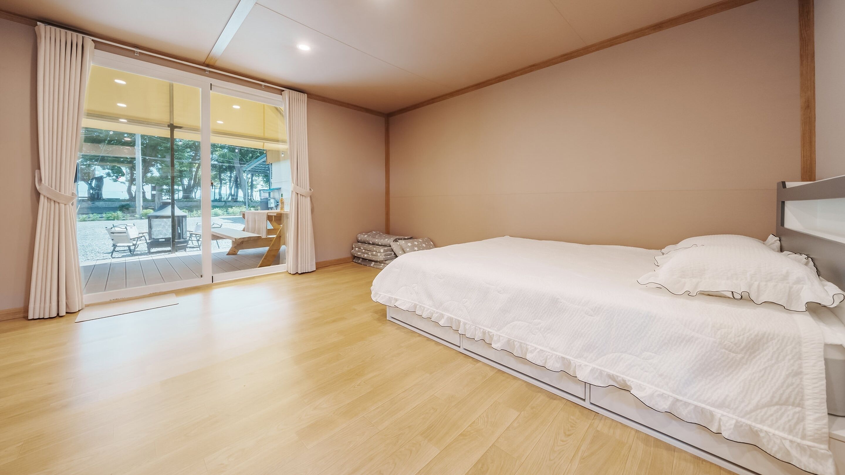 A bedroom with a large bed, a sliding glass door leading to an outdoor area, and a wooden floor.
