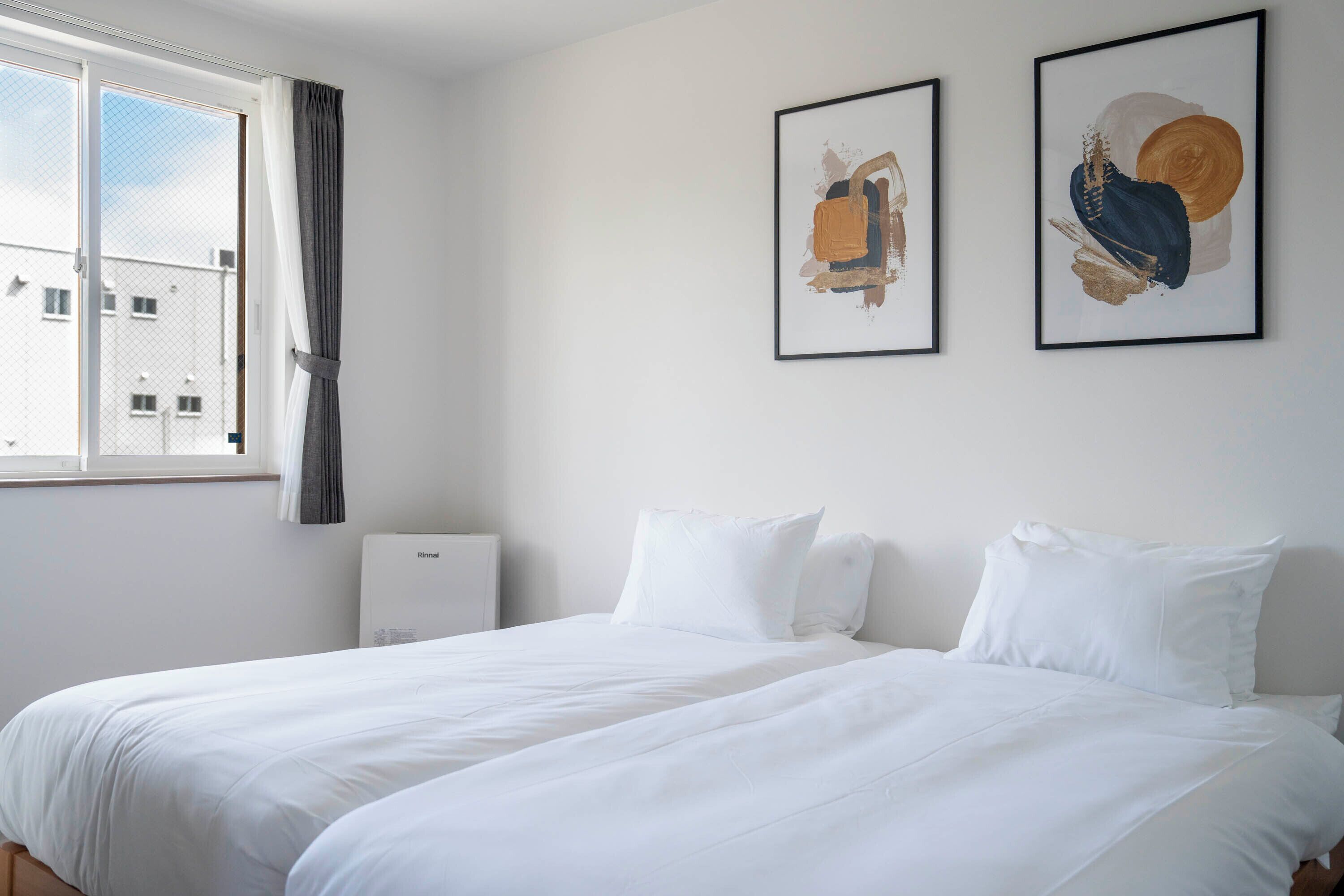 A hotel room with a bed, two framed artworks, a radiator, and a window with curtains.