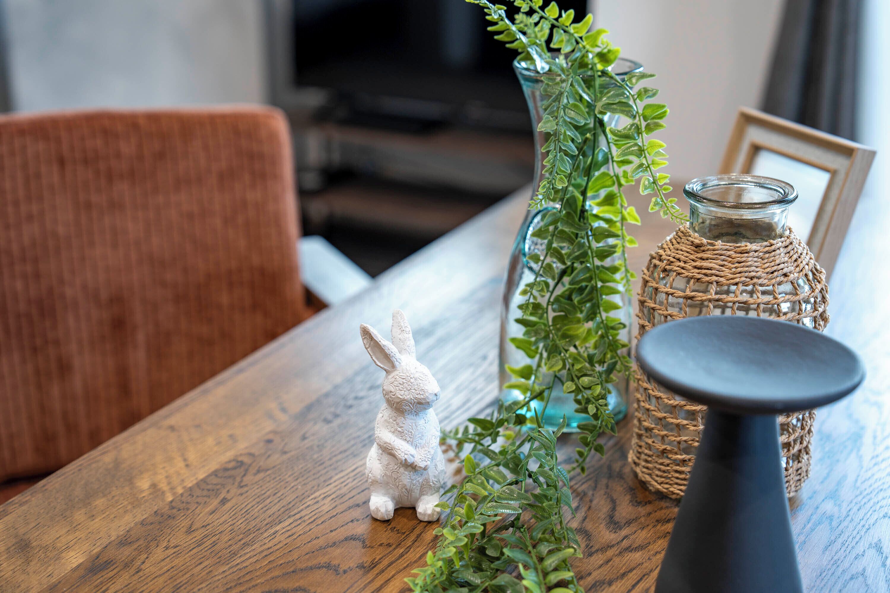 Una mesa de madera con un florero de vidrio, una cesta de mimbre y una pequeña figura de conejo blanco.