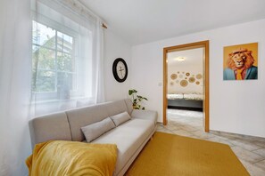 A room with a sofa, a yellow rug, a clock, a lion painting, and a door leading to another room.