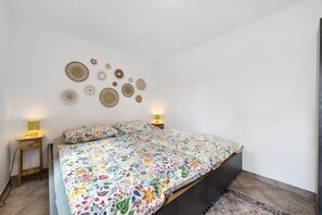 A bedroom with a floral bedspread, a bedside table with a lamp, and wall decor.