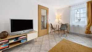 A living room with a television, bookshelf, dining area, and a window with curtains. - Apartment 'Malia' with Shared Terrace, Shared Garden and Wi-Fi (Neubulach)