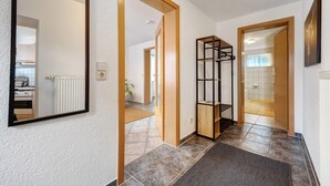 A hallway with a mirror, wooden doors, a black metal shelf, and a tiled floor. - Apartment 'Malia' with Shared Terrace, Shared Garden and Wi-Fi (Neubulach)