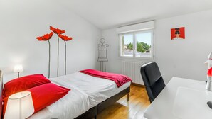 A bedroom with a bed, red pillows, a bedside lamp, a window, and a chair. - Villa Safari Golf & Spa - Toulouse - prox. Airbus (Plaisance-du-Touch)
