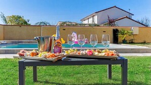 A poolside table with a wine bottle, glasses, and a charcuterie board. - Villa Safari Golf & Spa - Toulouse - prox. Airbus (Plaisance-du-Touch)