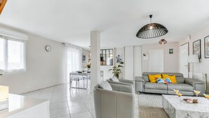 A modern living room with a grey sofa, a marble coffee table, and a dining area in the background. - Villa Safari Golf & Spa - Toulouse - prox. Airbus (Plaisance-du-Touch)