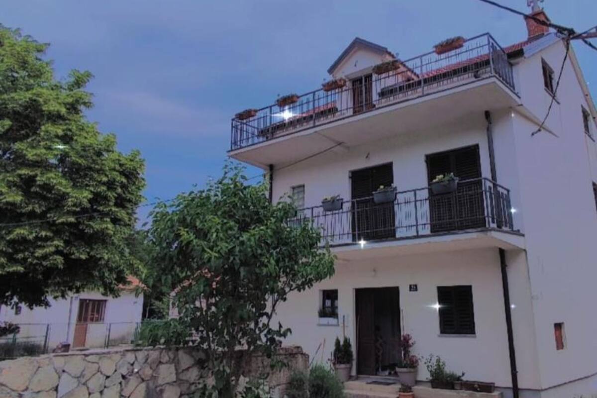 Un edificio de dos pisos con balcones, una pared de piedra y plantas en macetas.