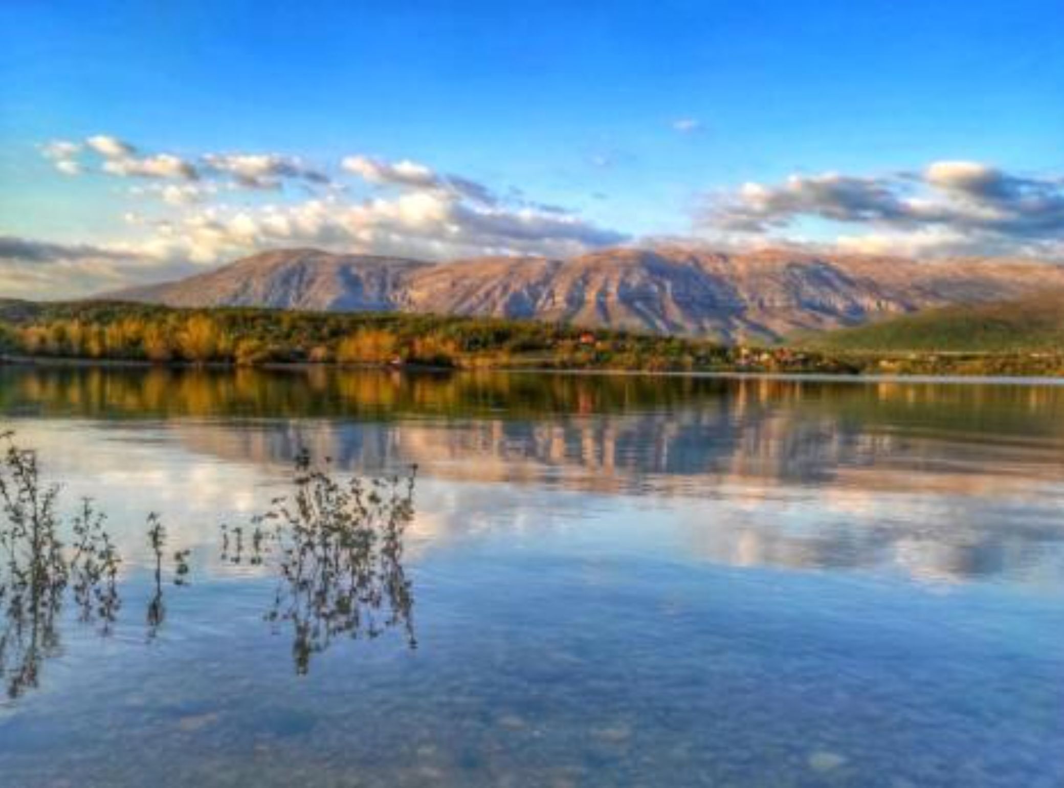 A calm lake with mountains in the background and clear skies.