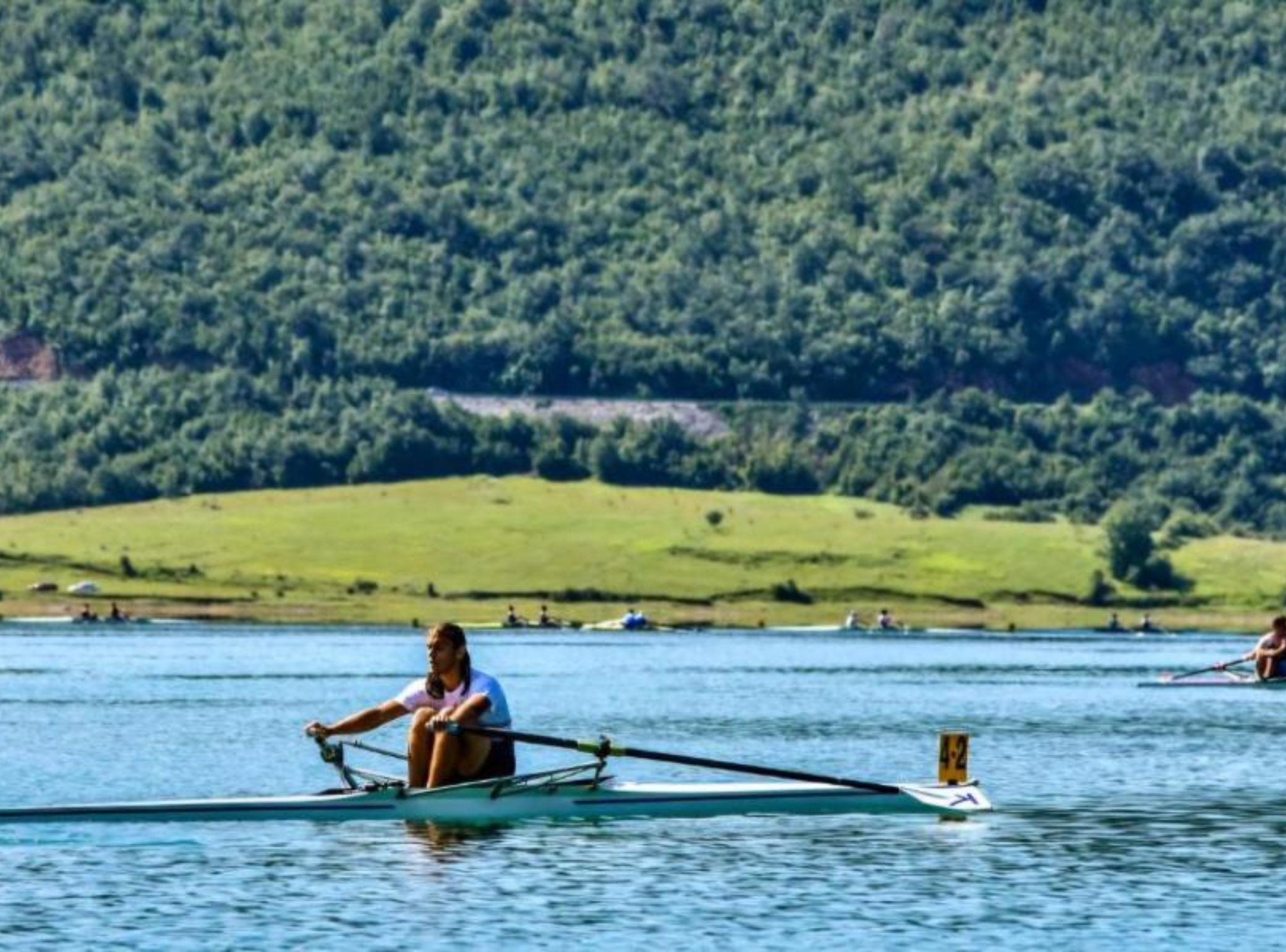 Una barca a remi su un lago calmo con un pendio boscoso sullo sfondo.