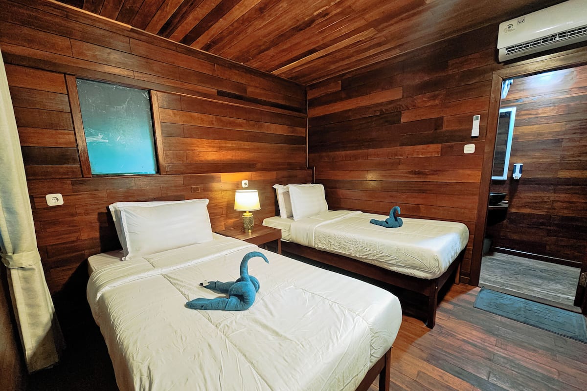 A room with two beds, wooden walls, a nightstand with a lamp, and a swan-shaped decoration on the beds.