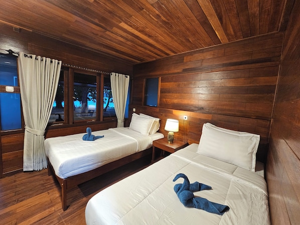 A room with two beds, wooden walls, and a window with curtains.