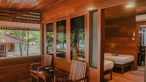 A wooden cabin with a dining area, two beds, and large windows offering a view of the outdoors. - ANDAU DIVE RESORT - RAJA AMPAT (Miosandau Kecil Island)