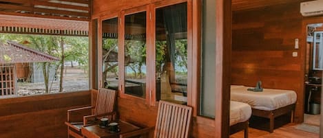 A wooden cabin with a dining area, two beds, and large windows offering a view of the outdoors.