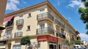 Un edificio de varios pisos con balcones, un letrero rojo que dice 'el jamón' y un cielo azul despejado.