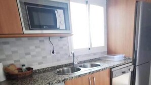 Una cocina con armarios de madera, microondas, lavadora, pileta y refrigerador.