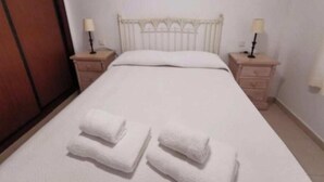 Una cama individual con cabecera blanca y dos mesitas de noche con lámparas. Hay dos toallas enrolladas sobre la cama.