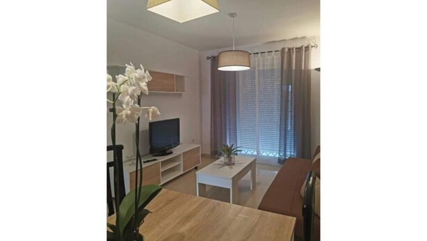 Una sala de estar con televisor, una mesa de centro y una planta.