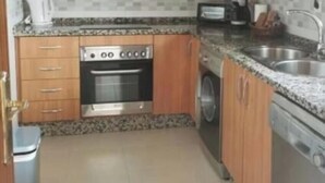 Cocina compacta con armarios de madera, microondas integrado, estufa y lavavajillas.