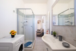Ein modernes Badezimmer mit einer gläsernen Duschkabine, einem großen Waschbecken und einer Waschmaschine.