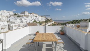 Una terraza en la azotea con una mesa y sillas de madera, con vistas a un pueblo encalado de tejados terracota.