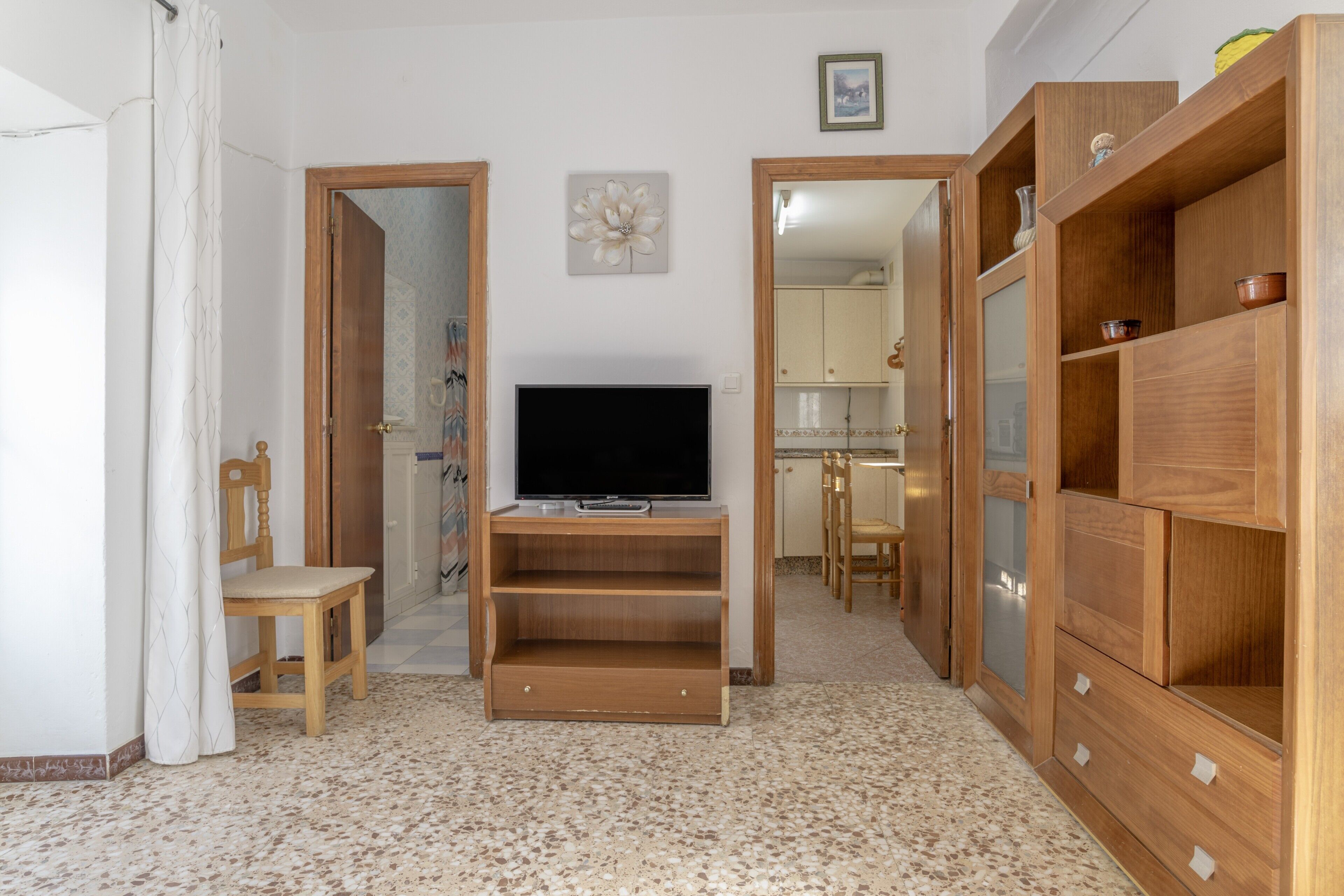 A room with a television on a wooden stand, a chair, a cabinet, and a door leading to another room.