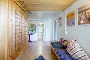 A hallway with a wooden wall, a metal rack, a sofa with patterned cushions, and framed artwork on the wall.