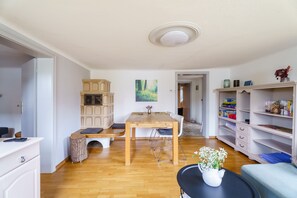Une pièce comprenant une table à manger en bois, des chaises blanches, une petite table ronde avec un vase et une bibliothèque.