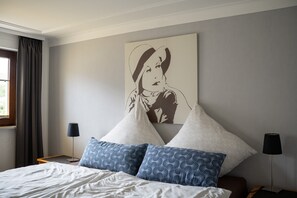 Une chambre d’hôtel avec un lit, des oreillers, une table de chevet, une lampe, une fenêtre avec des rideaux et un mur orné d’un tableau.