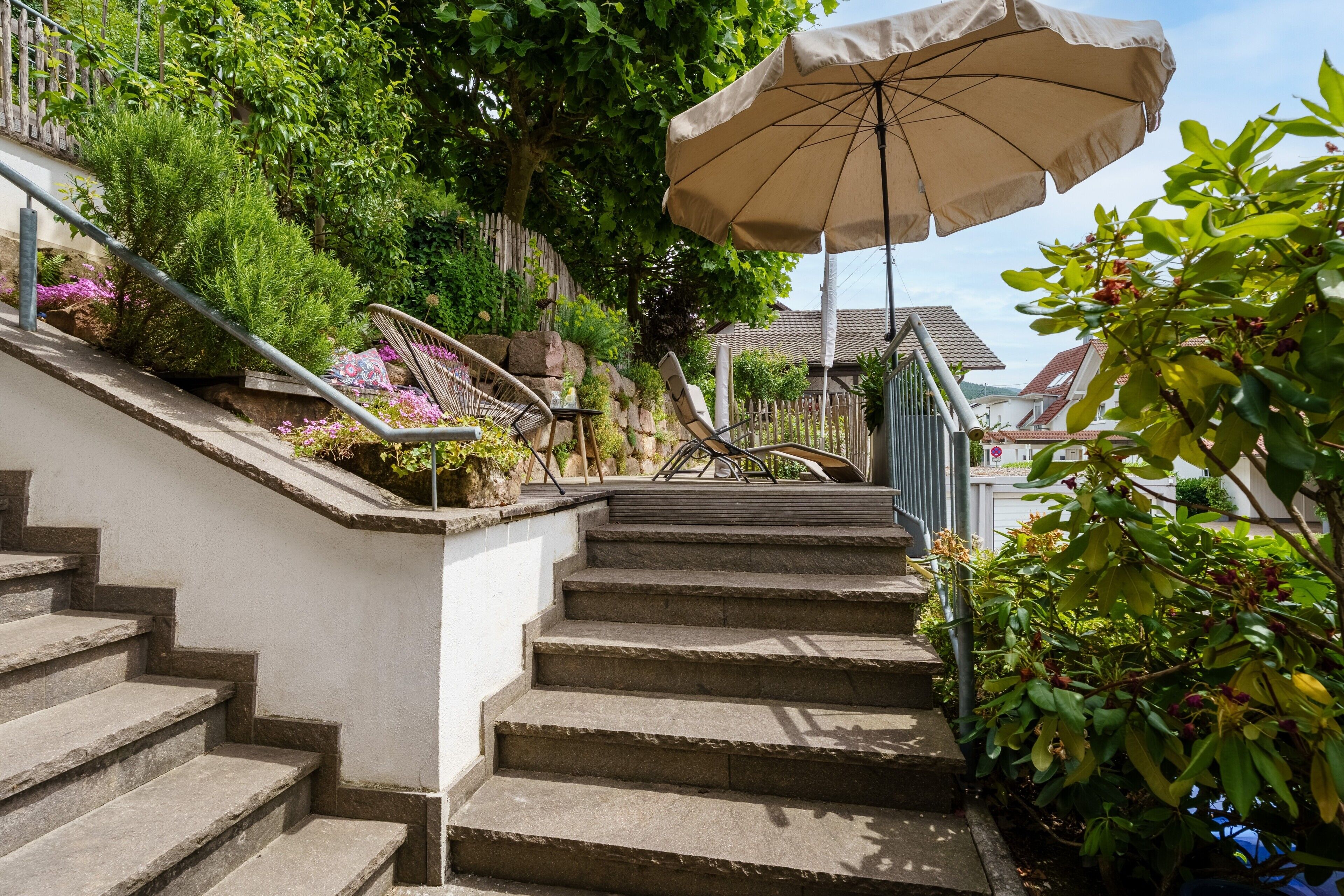 Un escalier en pierre menant à une maison dotée d’un jardin, d’une rambarde en métal et d’un grand parasol.