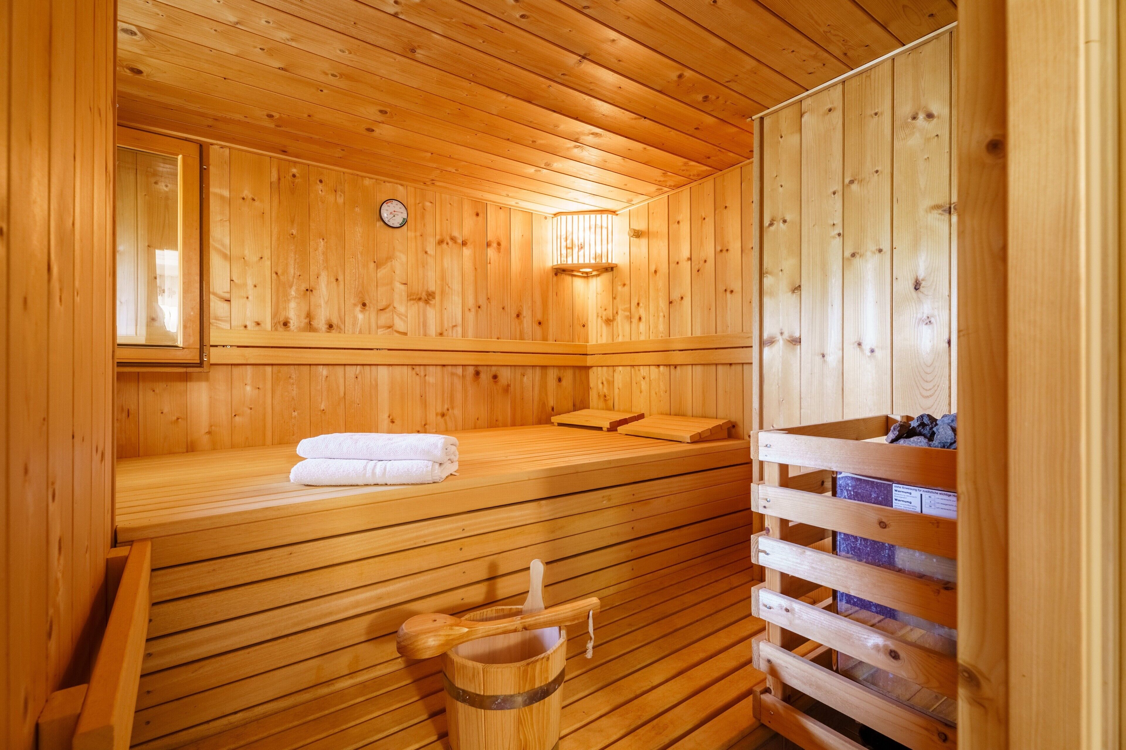 Un sauna en bois avec des bancs, une horloge fixée au mur et un seau en bois.