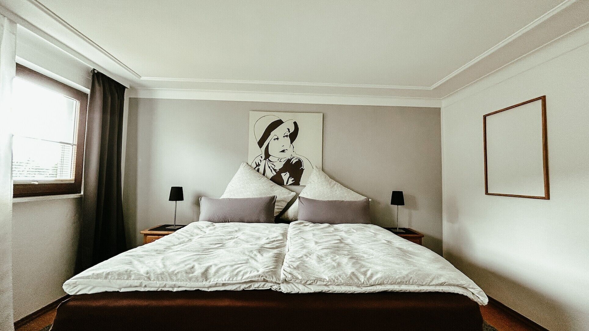 Une chambre d’hôtel avec un grand lit, deux tables de chevet avec des lampes, une fenêtre avec des rideaux et un tableau accroché au mur.