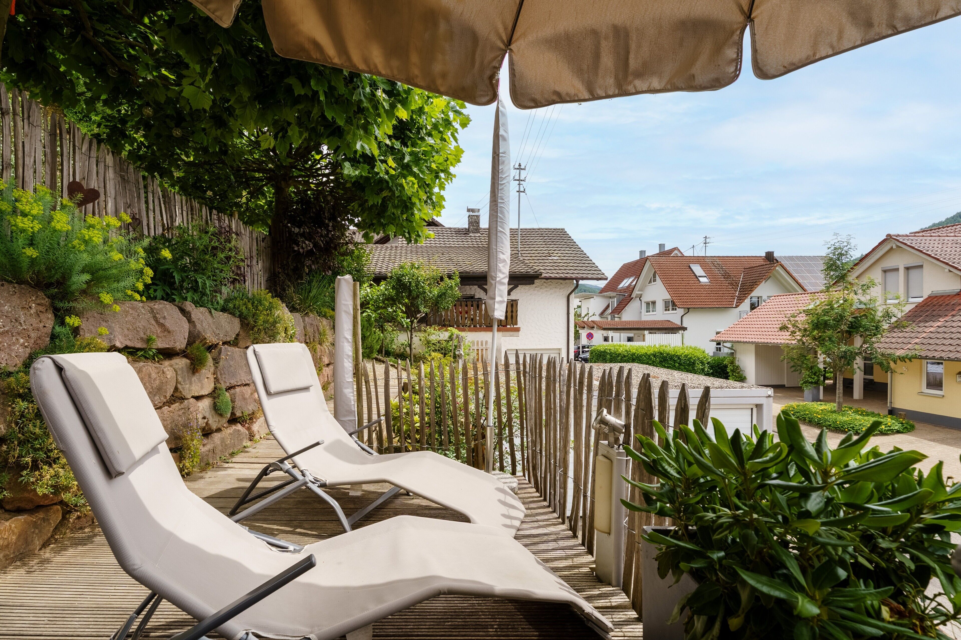 A balcony with two lounge chairs, a wooden fence, and a view of houses.