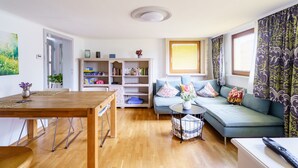 A living room with a wooden dining table, a sofa with cushions, a bookshelf, and a window with curtains. - Holiday Apartment 'Silvi und Heinz Huber' in Durbach, Traditional Timber-Framed House (Durbach)