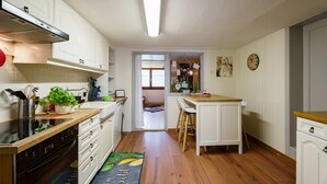 A kitchen with white cabinets, a stove, a sink, and a wooden countertop. There is a window with blinds, a door leading to another room, and a clock on the wall. - Holiday Apartment 'Silvi und Heinz Huber' in Durbach, Traditional Timber-Framed House (Durbach)