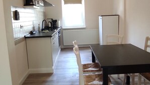 A modern kitchen with white cabinets, a black countertop, and a dining area with a black table and wicker chairs. - Apartment Wernerstr in the center - 3 bedrooms (Cottbus)