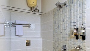 A bathroom with a toilet, a shower, and a tiled wall with a hand dryer and soap dispenser. - Emerald Suites By Classio (Bengaluru)
