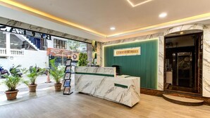 A hotel reception area with a marble reception desk, green wall, and a clock. - Emerald Suites By Classio (Bengaluru)