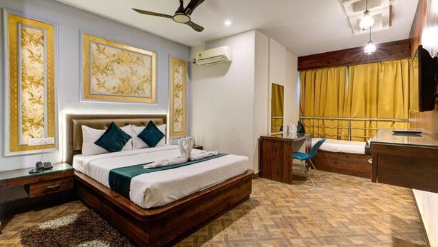 A hotel room with a bed, a desk, a chair, a mirror, and a ceiling fan. - Emerald Suites By Classio (Bengaluru)